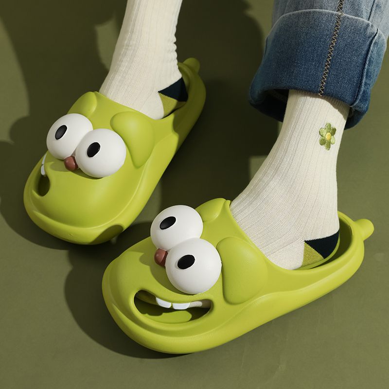 Green cartoonish slippers with large white eyes worn by a person on a green background