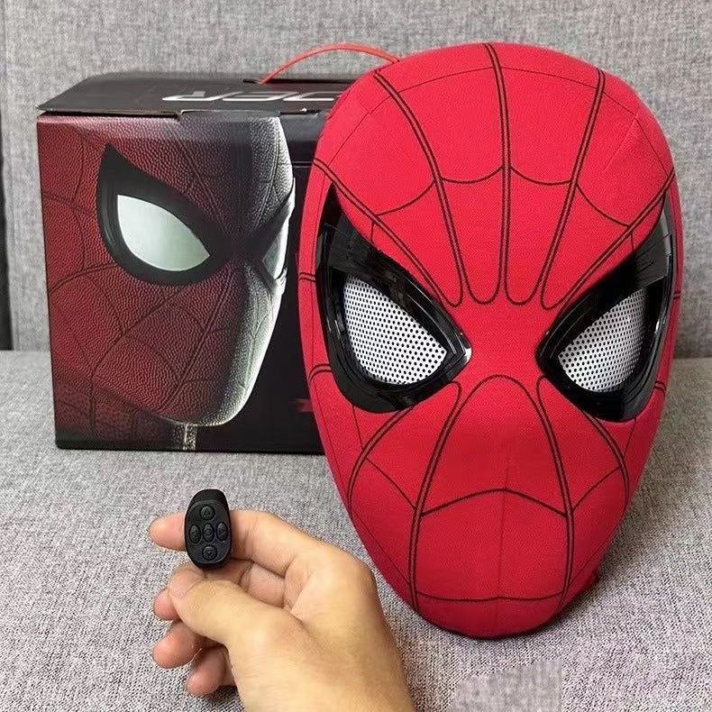 Red superhero mask with black web patterns held by a hand, next to a box with a similar design.